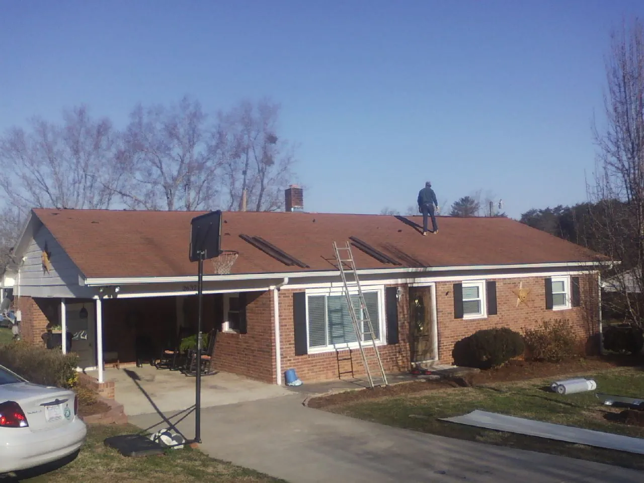 Roofer stripping a shingle roof on a brick ranch before metal panels in Fredericksburg